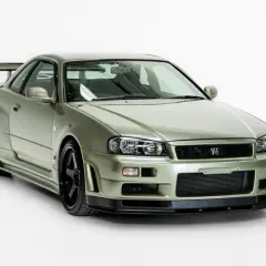 Kultowy Nissan Skyline R34 w kolorze oliwkowym, z czarnymi felgami i charakterystycznym spojlerem, gotowy do podboju dróg.