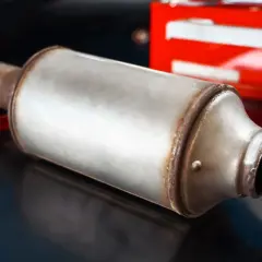 Metalowy tłumik, element układu wydechowego, prawdopodobnie dpf w benzynie, leży na ciemnym tle.