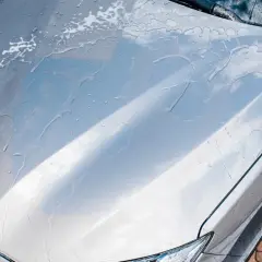 Krople wody i piany na masce srebrnego auta. Czy po woskowaniu auto trzeba płukać?