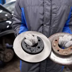 Mechanik prezentuje nowy i zardzewiały hamulcowy tarcz, pokazując potrzebę czyszczenia tarcz hamulcowych.