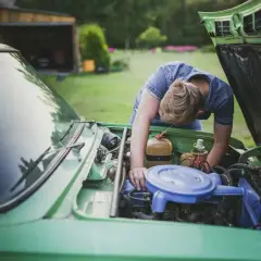 Mężczyzna pochyla się nad silnikiem zielonego samochodu, sprawdzając, jak sprawdzić czy odma jest sprawna.