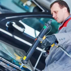 Mechanik aplikuje uszczelniacz na szybę samochodu. Pytanie: czym smarować uszczelki w aucie? Odpowiedź: specjalistycznym preparatem.