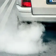 Gęsty, biały dym z wydechu diesel otacza tył samochodu na drodze.