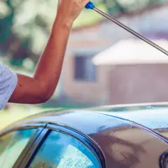 Mężczyzna pokazuje, jak myć auto na myjni, używając myjki ciśnieniowej do spłukiwania dachu samochodu.