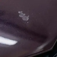 Na ciemnej masce samochodu widoczne są drobne odpryski lakieru i ślady po wodzie.