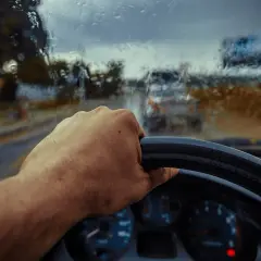 Deszczowa pogoda, ręka na kierownicy, a auto nie odpala. Widać deszcz na szybie i inne samochody w oddali.