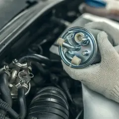 Ręce w rękawiczkach trzymają nowy filtr paliwa, gotowy do wymiany w samochodzie.