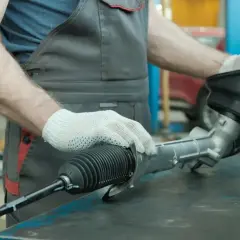 Mechanik w białych rękawiczkach sprawdza maglownicę, szukając luzu.