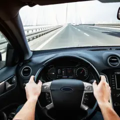 Ręce na kierownicy, jadąc przez most. Prędkościomierz pokazuje 130 km/h.
