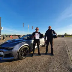 Dwóch mężczyzn z kaskami i certyfikatem po udanym kursie jazdy ekstremalnej obok sportowego samochodu.