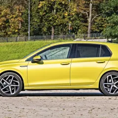 Żółty hatchback, czyli samochód z podnoszoną tylną klapą, zaparkowany na tle zieleni i drzew.