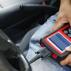 Diagnostyka komputerowa samochodu: mechanik podłącza skaner do złącza OBD w aucie, by sprawdzić jego stan techniczny.