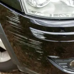 Widoczne liczne rysy na czarnym zderzaku plastikowym, wymagające naprawy.