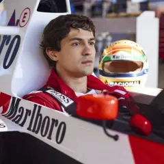 Młody kierowca w bolidzie, gotowy do startu w filmie o wyścigach samochodowych. Obok kask z logiem Marlboro.