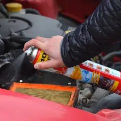 Ręka trzyma puszkę z preparatem samostart do diesla, rozpylając go w pobliżu filtra powietrza w silniku samochodu.