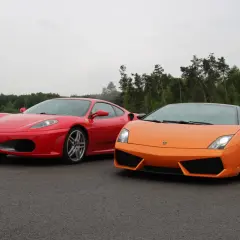 Czerwone Ferrari i pomarańczowe Lamborghini stoją obok siebie na torze wyścigowym, gotowe do rywalizacji.