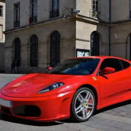 Czerwone włoskie auto sportowe Ferrari F430 na brukowanej ulicy przed zabytkową kamienicą.