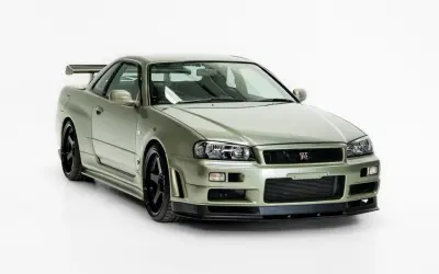 Kultowy Nissan Skyline R34 w kolorze oliwkowym, z czarnymi felgami i charakterystycznym spojlerem, gotowy do podboju dróg.