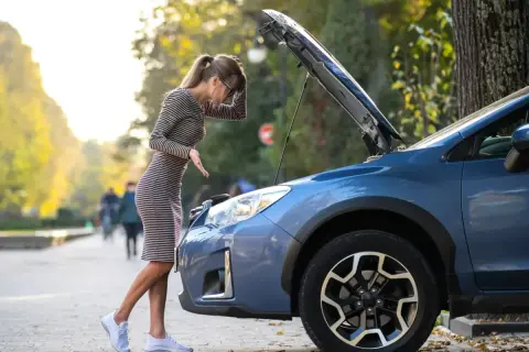 Kobieta zmartwiona patrzy pod maskę auta, szukając przyczyn problemów. Czy to objawy awarii pompy paliwa?