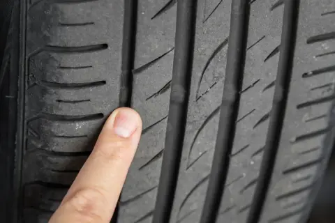 Palec wskazujący na bieżniku opony, uwidaczniający drobne mikropęknięcia.