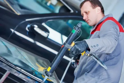 Mechanik aplikuje uszczelniacz na szybę samochodu. Pytanie: czym smarować uszczelki w aucie? Odpowiedź: specjalistycznym preparatem.