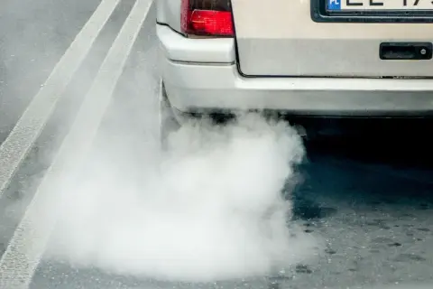Gęsty, biały dym z wydechu diesel otacza tył samochodu na drodze.