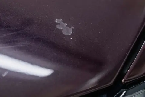 Na ciemnej masce samochodu widoczne są drobne odpryski lakieru i ślady po wodzie.