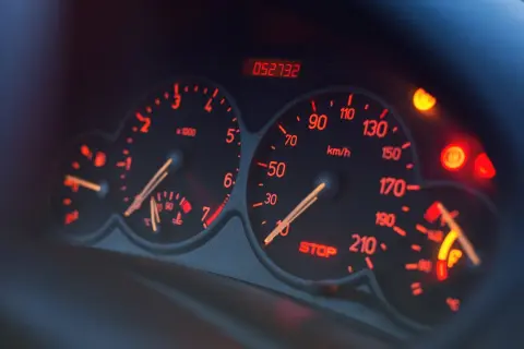 Deska rozdzielcza samochodu z podświetlanymi na czerwono wskaźnikami. Widoczny obrotomierz, prędkościomierz, wskaźnik paliwa i kontrolki. Czy to EPC?