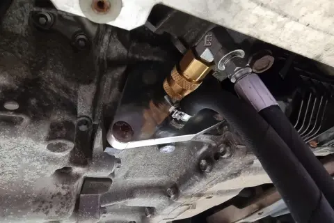 Metalowy adapter z szybkozłączką do dynamicznej wymiany oleju w skrzyni biegów, podłączony do węży.