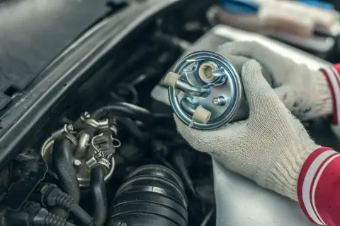 Ręce w rękawiczkach trzymają nowy filtr paliwa, gotowy do wymiany w samochodzie.