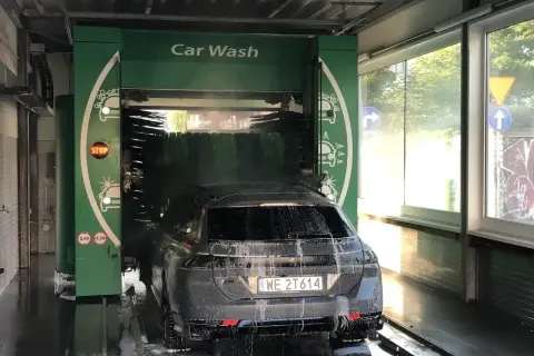 Czarnym autem wjeżdżamy do myjni automatycznej. Piana i szczotki skutecznie usuwają brud, pokazując, czym umyć auto.