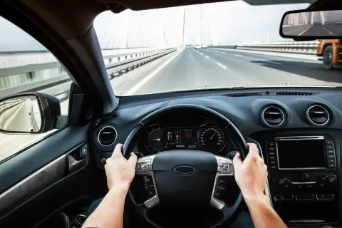 Ręce na kierownicy, jadąc przez most. Prędkościomierz pokazuje 130 km/h.