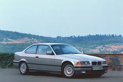 Srebrne BMW E36 coupe, idealne auto do driftu, stoi na tle malowniczego krajobrazu Toskanii.