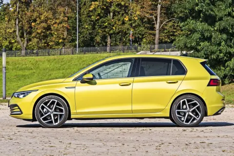Żółty hatchback, czyli samochód z podnoszoną tylną klapą, zaparkowany na tle zieleni i drzew.