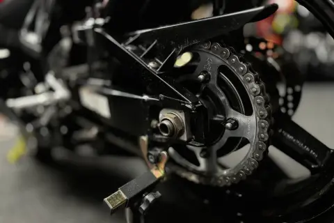 Zbliżenie na tylne koło motocykla z widocznym łańcuchem i zębatką, gotowe do czyszczenia łańcucha motocyklowego.