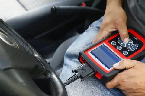 Diagnostyka komputerowa samochodu: mechanik podłącza skaner do złącza OBD w aucie, by sprawdzić jego stan techniczny.