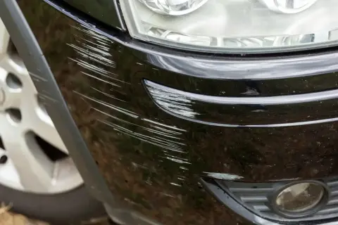Widoczne liczne rysy na czarnym zderzaku plastikowym, wymagające naprawy.