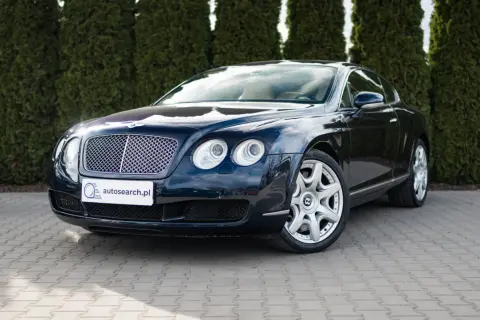 Elegancki, ciemnogranatowy Bentley Continental GT, brytyjski producent luksusowych aut, zaparkowany przed żywopłotem.