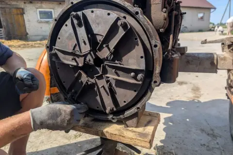 Mechanik w rękawiczkach reguluje mechanizm sprzęgła, przygotowując traktor do pracy.