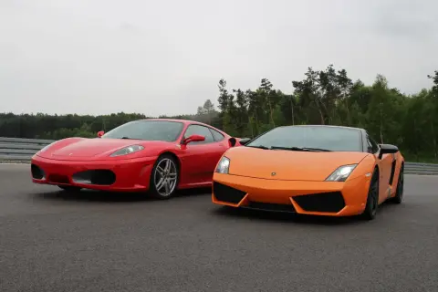 Czerwone Ferrari i pomarańczowe Lamborghini stoją obok siebie na torze wyścigowym, gotowe do rywalizacji.