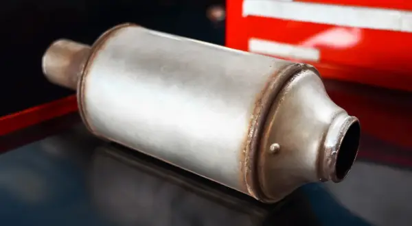 Metalowy tłumik, element układu wydechowego, prawdopodobnie dpf w benzynie, leży na ciemnym tle.