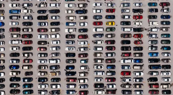Wielki parking pełen europejskich marek samochodów, uporządkowanych w rzędach.