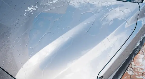 Krople wody i piany na masce srebrnego auta. Czy po woskowaniu auto trzeba płukać?