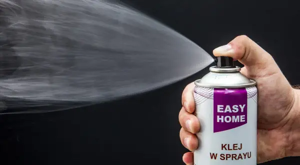 Dłoń trzyma puszkę z napisem "EASY HOME KLEJ W SPRAYU", rozpylając białą mgiełkę. Idealny do podsufitki.