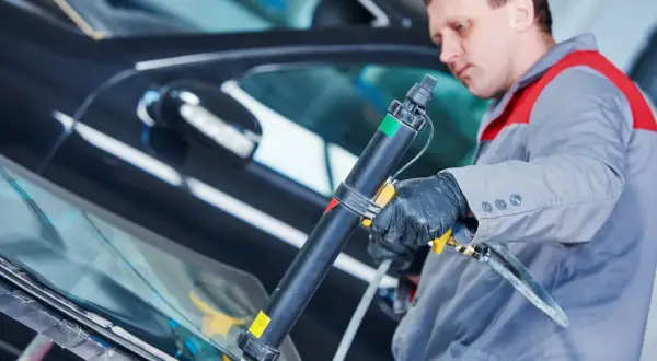 Mechanik aplikuje uszczelniacz na szybę samochodu. Pytanie: czym smarować uszczelki w aucie? Odpowiedź: specjalistycznym preparatem.