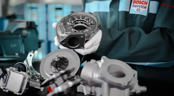 Mechanik w rękawiczkach pokazuje części turbosprężarki, kluczowego elementu, gdzie jest turbina w samochodzie.