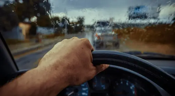 Deszczowa pogoda, ręka na kierownicy, a auto nie odpala. Widać deszcz na szybie i inne samochody w oddali.