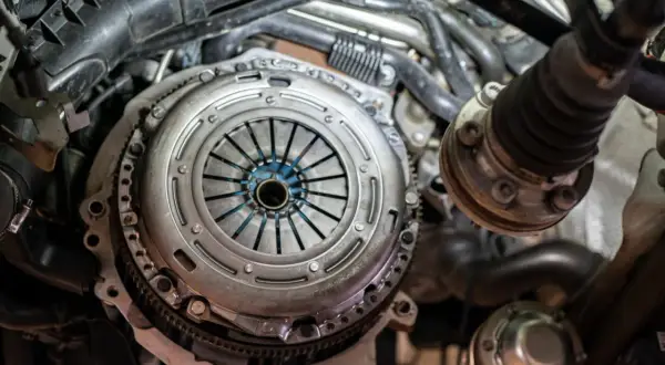 Mechanik pracuje nad grawitacyjnym odpowietrzaniem sprzęgła w samochodzie. Widoczny jest mechanizm sprzęgła i elementy silnika.
