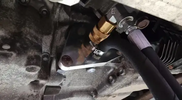 Metalowy adapter z szybkozłączką do dynamicznej wymiany oleju w skrzyni biegów, podłączony do węży.