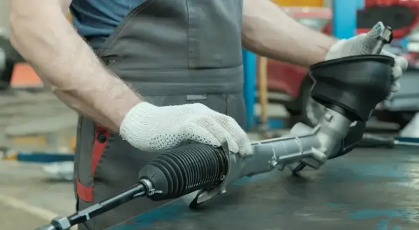 Mechanik w białych rękawiczkach sprawdza maglownicę, szukając luzu.